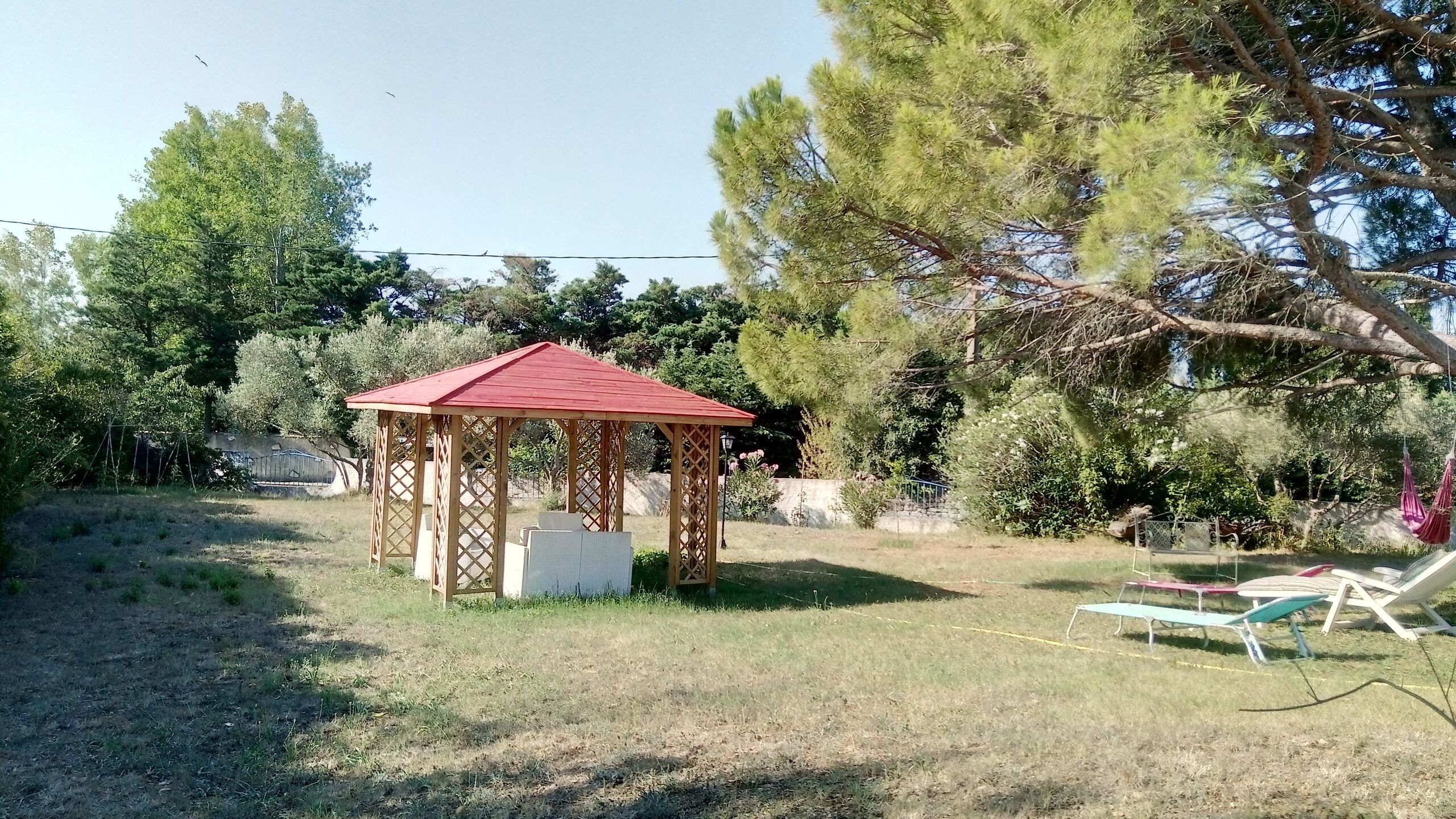 A gazebo with a red roof in a grassy area surrounded by trees.