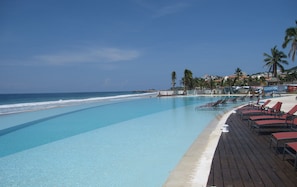 Un área junto a la piscina con sillones de descanso, una terraza de madera y vista al océano.