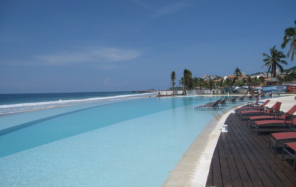 A poolside area with lounge chairs, a wooden deck, and a view of the ocean.