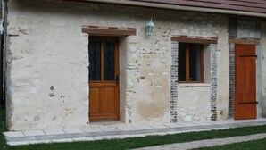 A rustic stone building with a red-tiled roof, two wooden doors, and a small window with a lantern above it.
