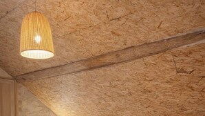 A bedroom with a wooden ceiling, a bed with white bedding, a hanging light fixture, and a wooden floor.