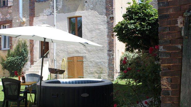 A hot tub in a backyard with a table and chairs, surrounded by a brick wall and a garden with roses.