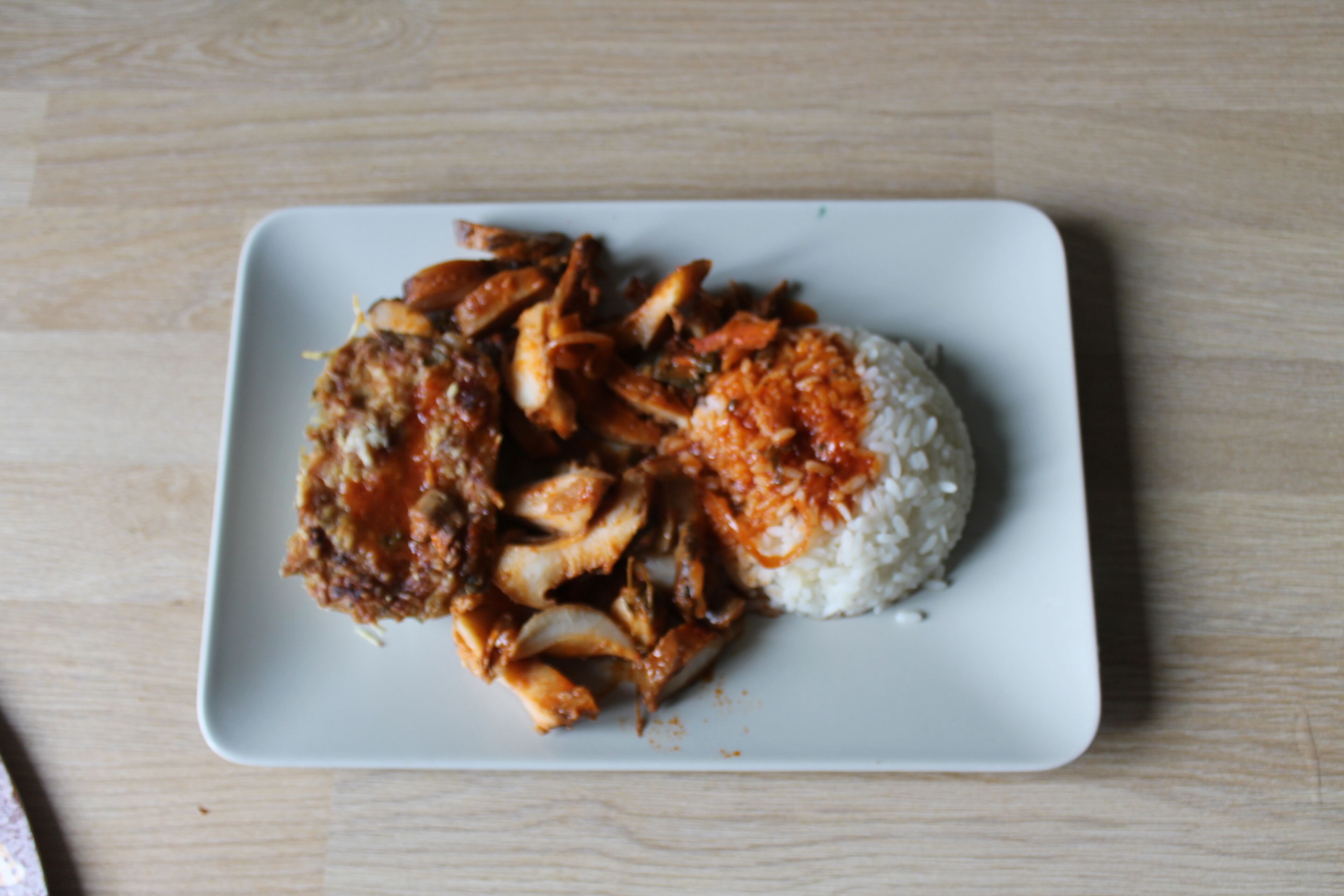 Un plato blanco cuadrado con arroz y pollo frito sobre una mesa de madera.