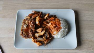 Un plato blanco cuadrado con arroz y pollo frito sobre una mesa de madera.