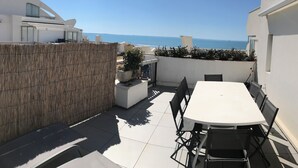 A patio with a white table and chairs, a bamboo fence, and a view of the sea.