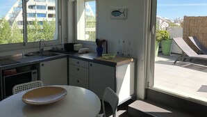 A modern kitchen with a dining area, large windows, and a view of buildings and greenery.