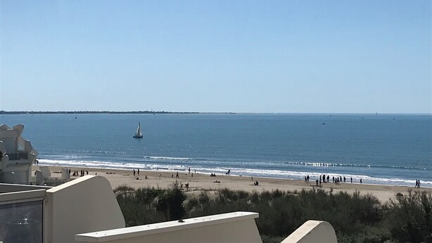 A beach view with a clear sky, a boat on the water, and people on the sand.