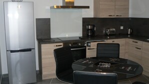 Una cocina moderna con refrigerador, estufa y cafetera. Hay una mesa de comedor con sillas.