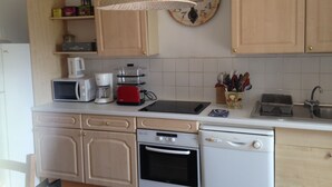 A kitchen with wooden cabinets, a microwave, a coffee maker, a toaster, a sink, and a clock on the wall. - Charming house, enclosed garden facing south, sheltered from the wind! (Arzon)
