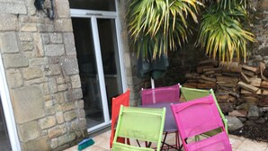 A patio area with a stone wall, a glass door, and a table with colorful chairs. - Charming house, enclosed garden facing south, sheltered from the wind! (Arzon)