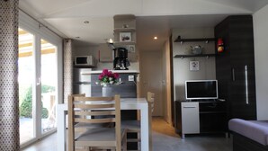 A modern kitchen with a dining area, a TV, and a sofa. - BEAUTIFUL AIR-CONDITIONED MOBILE HOME RENTAL 6-8 PEOPLE LA PALMYRE AUX CHARMETTES 4E (Les Mathes)