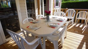 A covered outdoor dining area with a white table set for four, surrounded by white plastic chairs. - BEAUTIFUL AIR-CONDITIONED MOBILE HOME RENTAL 6-8 PEOPLE LA PALMYRE AUX CHARMETTES 4E (Les Mathes)