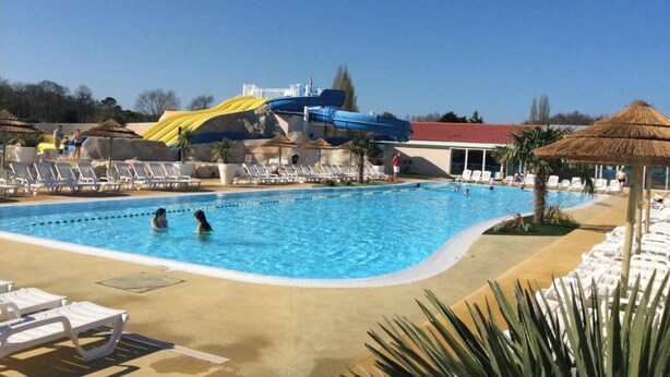 A swimming pool with lounge chairs, a water slide, and a thatched umbrella. - BEAUTIFUL AIR-CONDITIONED MOBILE HOME RENTAL 6-8 PEOPLE LA PALMYRE AUX CHARMETTES 4E (Les Mathes)