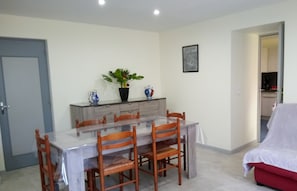 A dining area with a glass table, wooden chairs, a potted plant, and a cabinet.