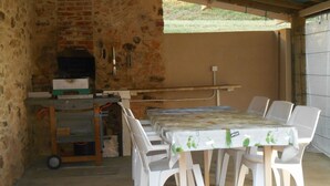 A covered outdoor dining area with a brick wall, a grill, and white plastic chairs and table. - perigourdine house in the countryside (saint germain de belves)