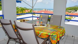 A balcony with a table set for two, a bottle of Cointreau, and a bottle of Bacardi. The balcony overlooks a coastal area with buildings and a view of the sea.