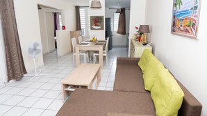 A compact living space with a sofa, a dining table with chairs, a small kitchen area, and a dining table with a fan.