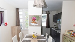 A modern kitchen with a dining area, featuring a light-colored tiled floor, a wooden dining table with white chairs, a hanging light fixture, and a kitchen counter with cabinets.