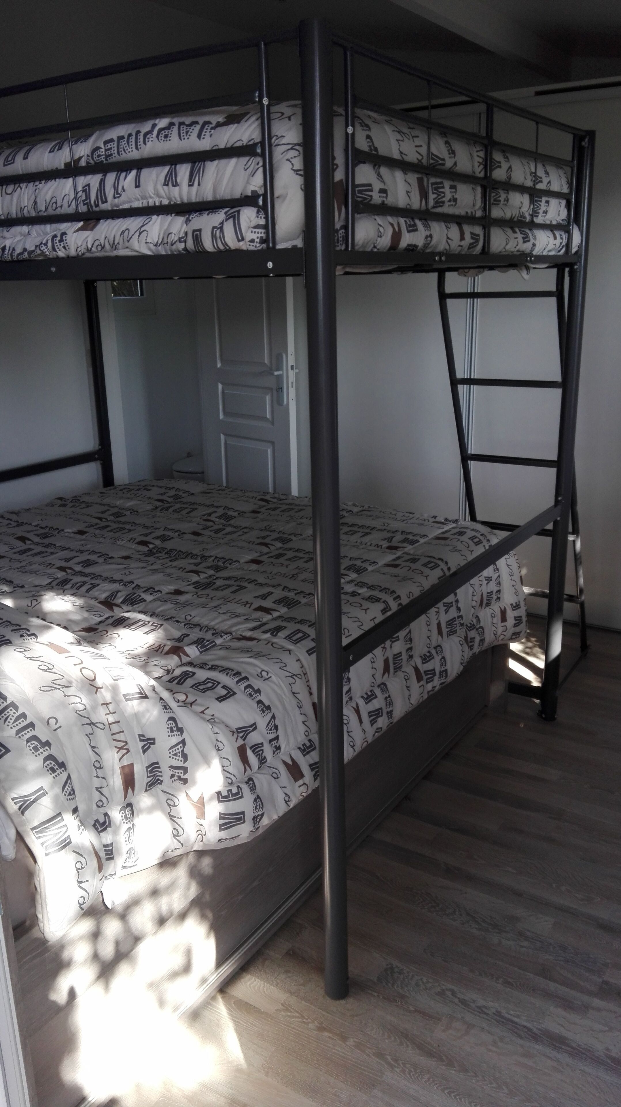 Un lit superposé avec une literie à motifs, une porte et un plancher en bois.