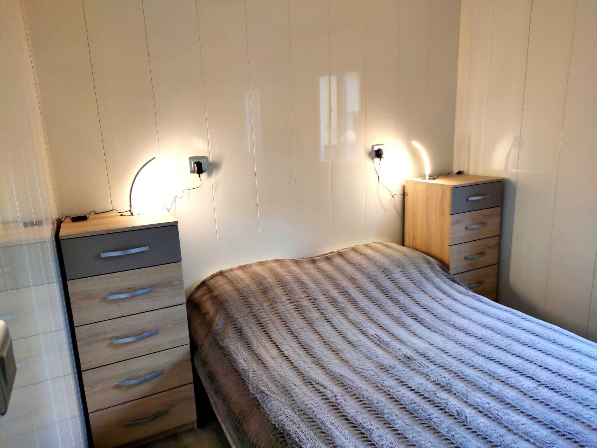 Et lille, pænt oplyst soveværelse med en seng, en kommode og to vægmonterede lamper.