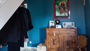 A staircase with white railings leading to a landing. Below, a wooden cabinet with drawers and a framed picture on the wall. A chair is positioned near the cabinet. - Homestay (Pontvallain)