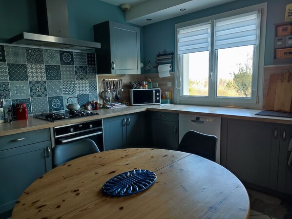 A kitchen with a round wooden table, a microwave, and a window with blinds.