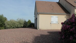 A house with a sloped roof, a gravel driveway, and a small garden with pink flowers. - Homestay (Pontvallain)