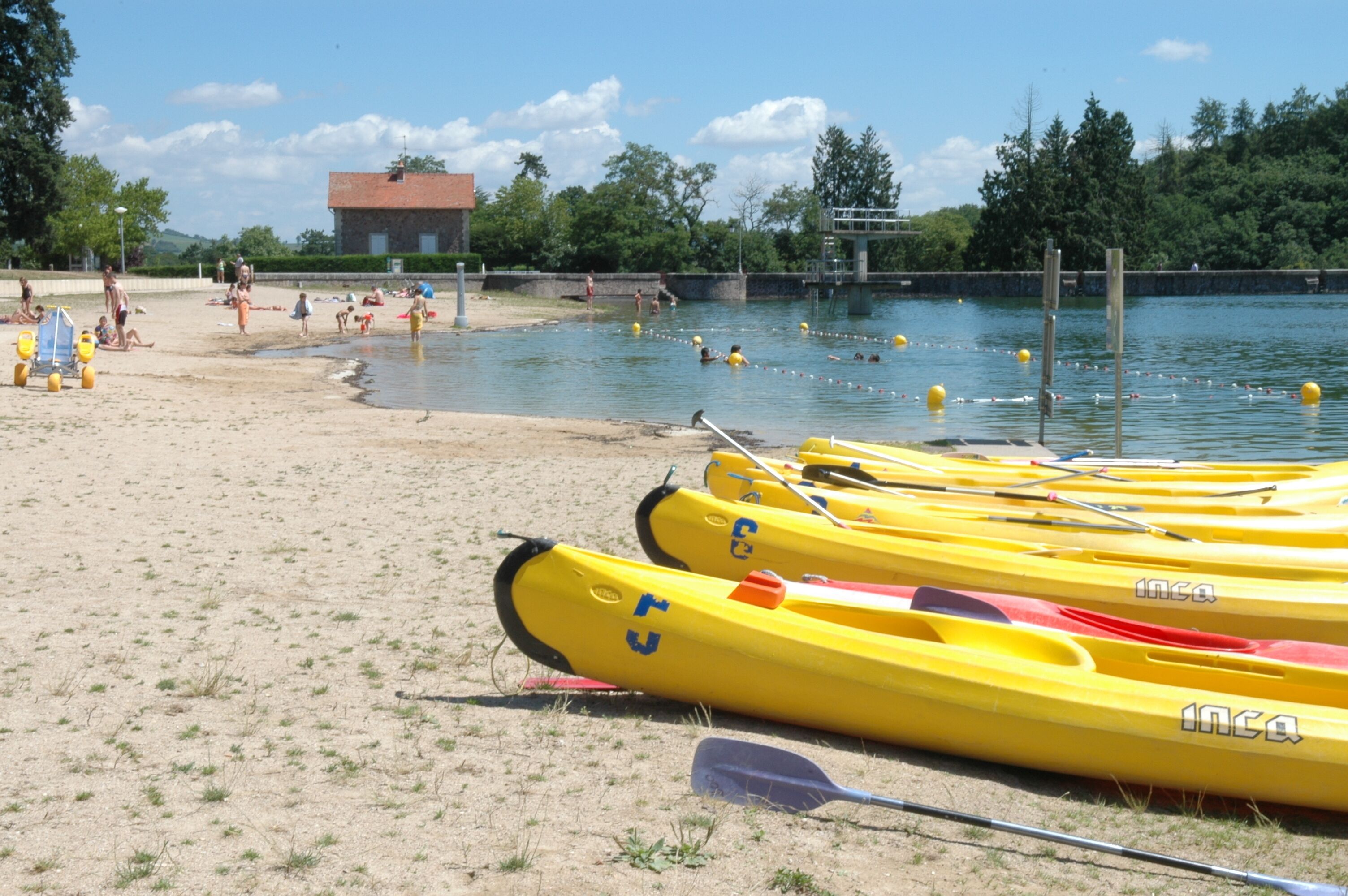 A beach with yellow kayaks lined up on the sand, a building in the background, and people in the water.
