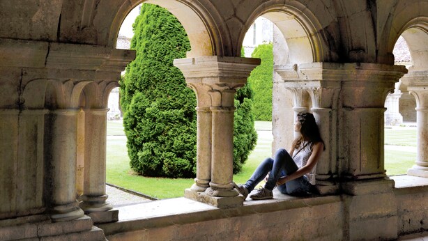 A stone architectural structure with arches and columns, a person sitting on a ledge, and a well-maintained green hedge in the background. - Near the castle of the Count of Bussy Rabutin (historical monument) studio 4 p (Bussy-Le-Grand)