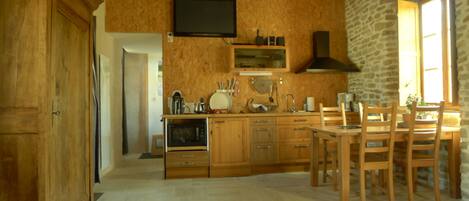 A kitchen with wooden cabinets, a built-in oven, a dining table with chairs, and a stone wall.