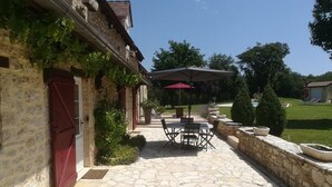 Une terrasse en pierre avec des meubles d’extérieur et un parasol rouge.
