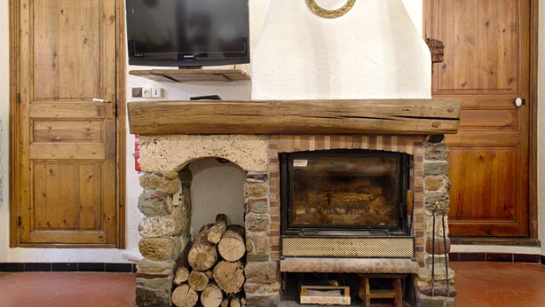 A fireplace with a stone surround, a television mounted above it, and wooden doors. - Apartment in the heart of the village (Puget-Théniers)