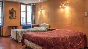 A hotel room with two beds, a small table, a chair, a mirror, and a radiator. - Apartment in the heart of the village (Puget-Théniers)
