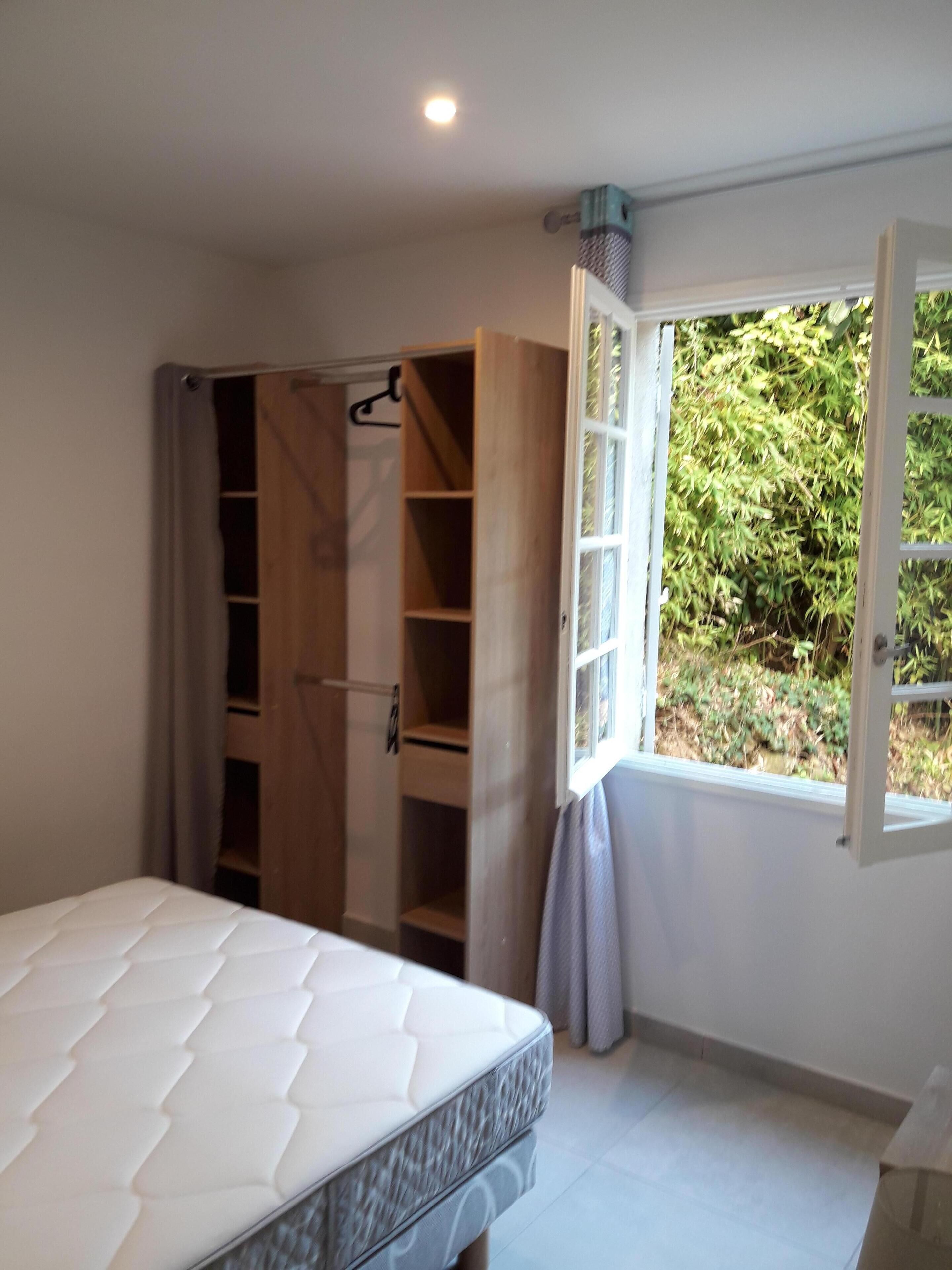 Quarto com uma cama, guarda-roupa de madeira e janela com vista para o verde.
