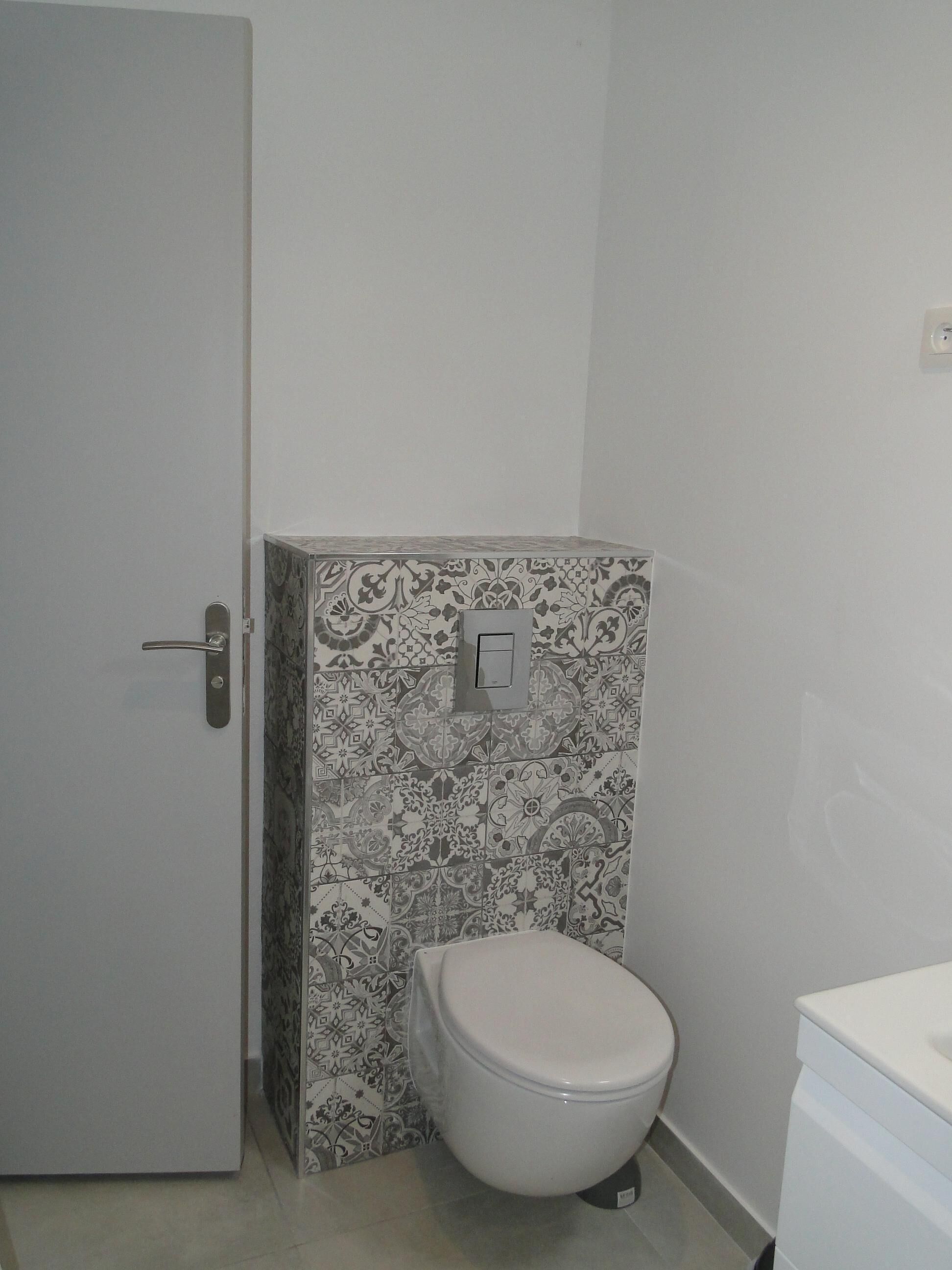 A small bathroom with a toilet, a door, and a wall with patterned tiles.