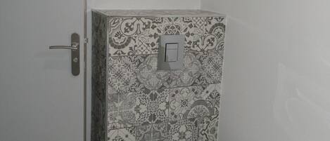 A small bathroom with a toilet, a door, and a wall with patterned tiles.