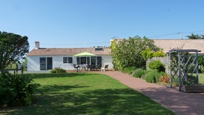 Una casa con techo de tejas, un patio con mobiliario exterior y un jardín.