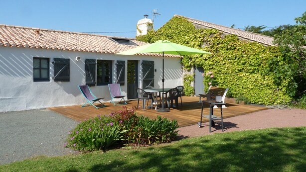 Una casa con techo de tejas, un porche cubierto con mobiliario exterior y un jardín con flores.