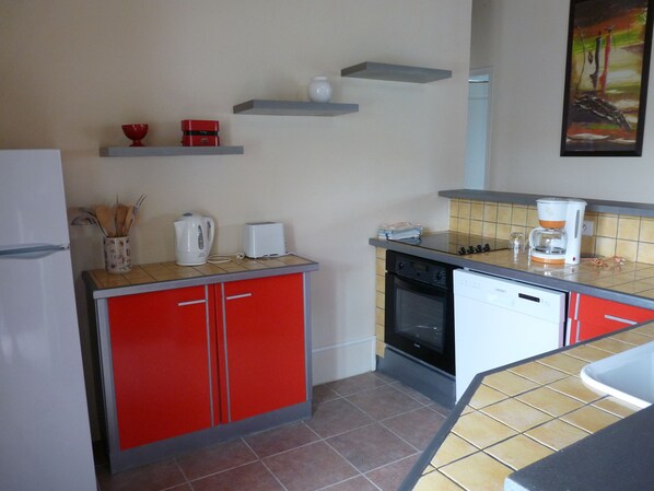 A compact kitchen with red cabinets, a white refrigerator, a coffee maker, and a dishwasher.