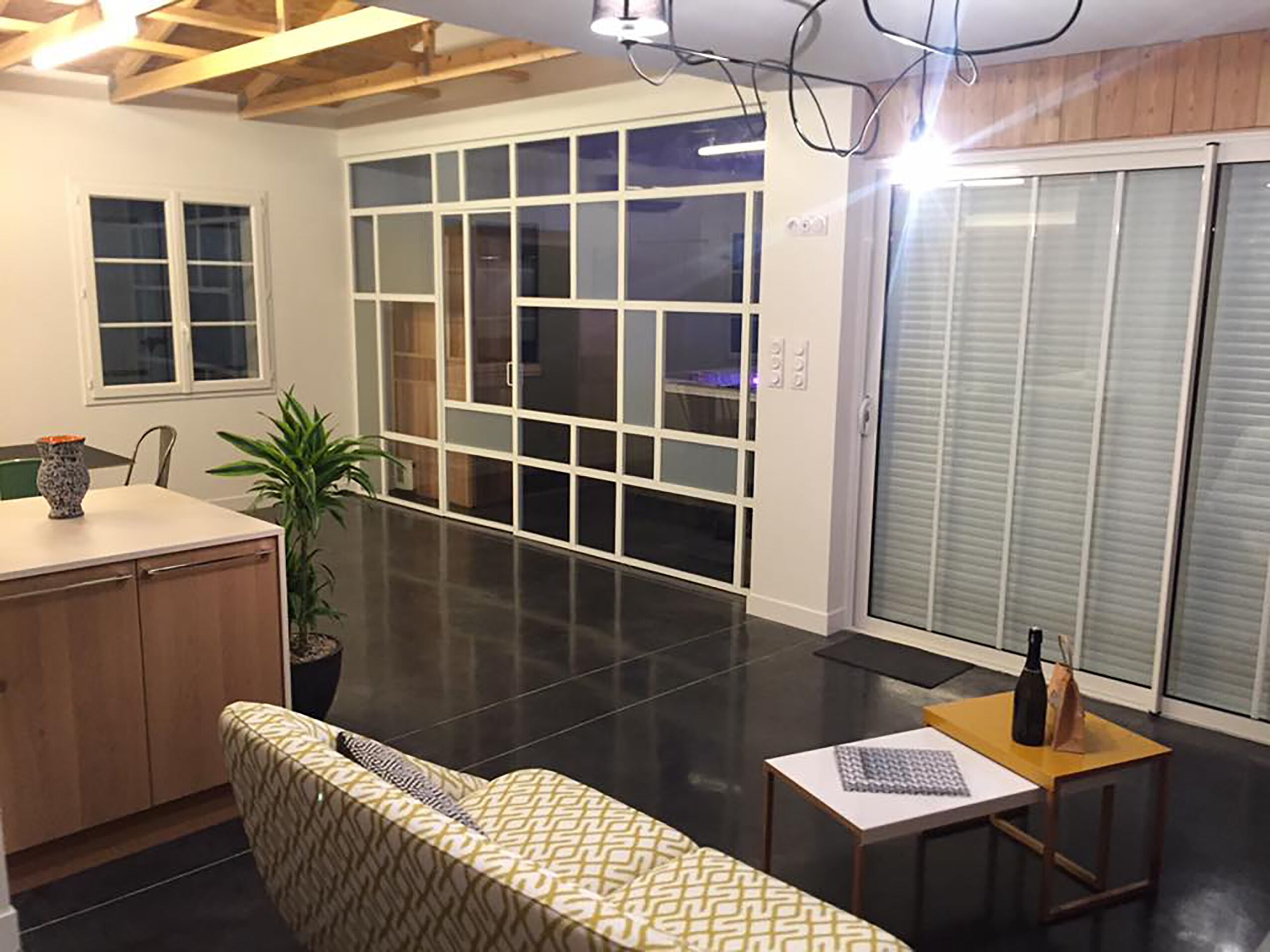 A modern interior with a sofa, a small table, a potted plant, and a sliding glass door leading to a balcony.