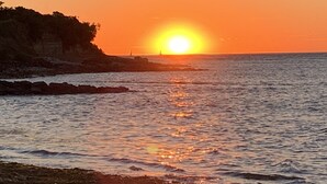 Solnedgang over en klippefyldt kystlinje med rolige vandflader, der spejler solen.