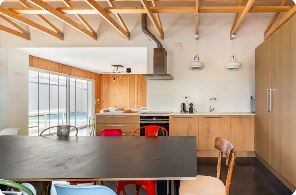 A modern kitchen with wooden cabinets, a black countertop, and a dining area with a table and chairs.