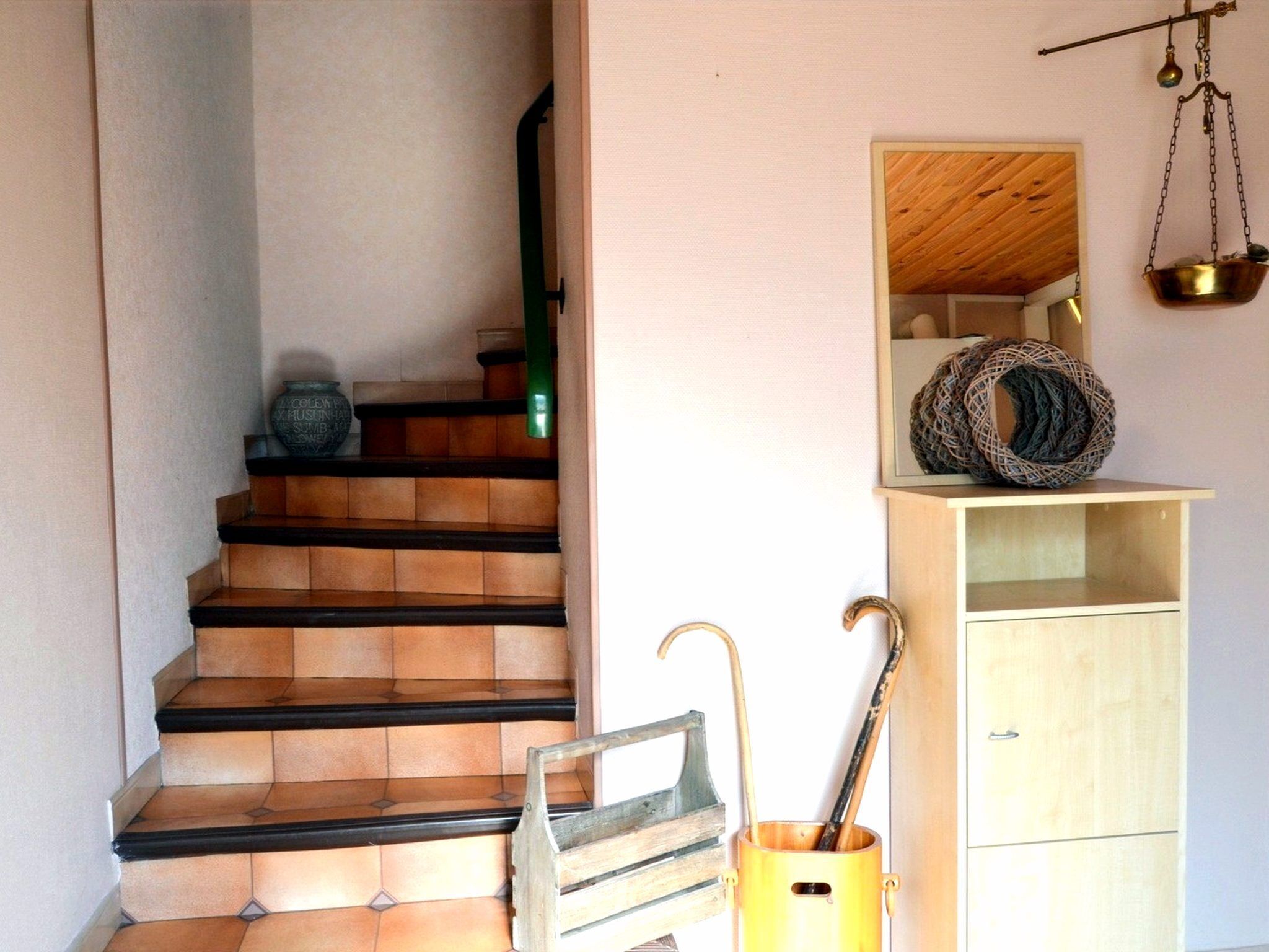 Una escala amb graons de fusta i barana metàl·lica, un armari de fusta amb una balança penjada, i una cistella de vimet sobre una prestatgeria.