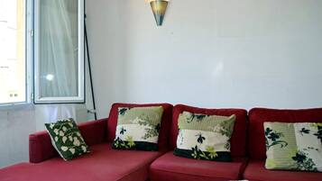 A red sofa with floral cushions, a white table with a document, and a wall-mounted light fixture.