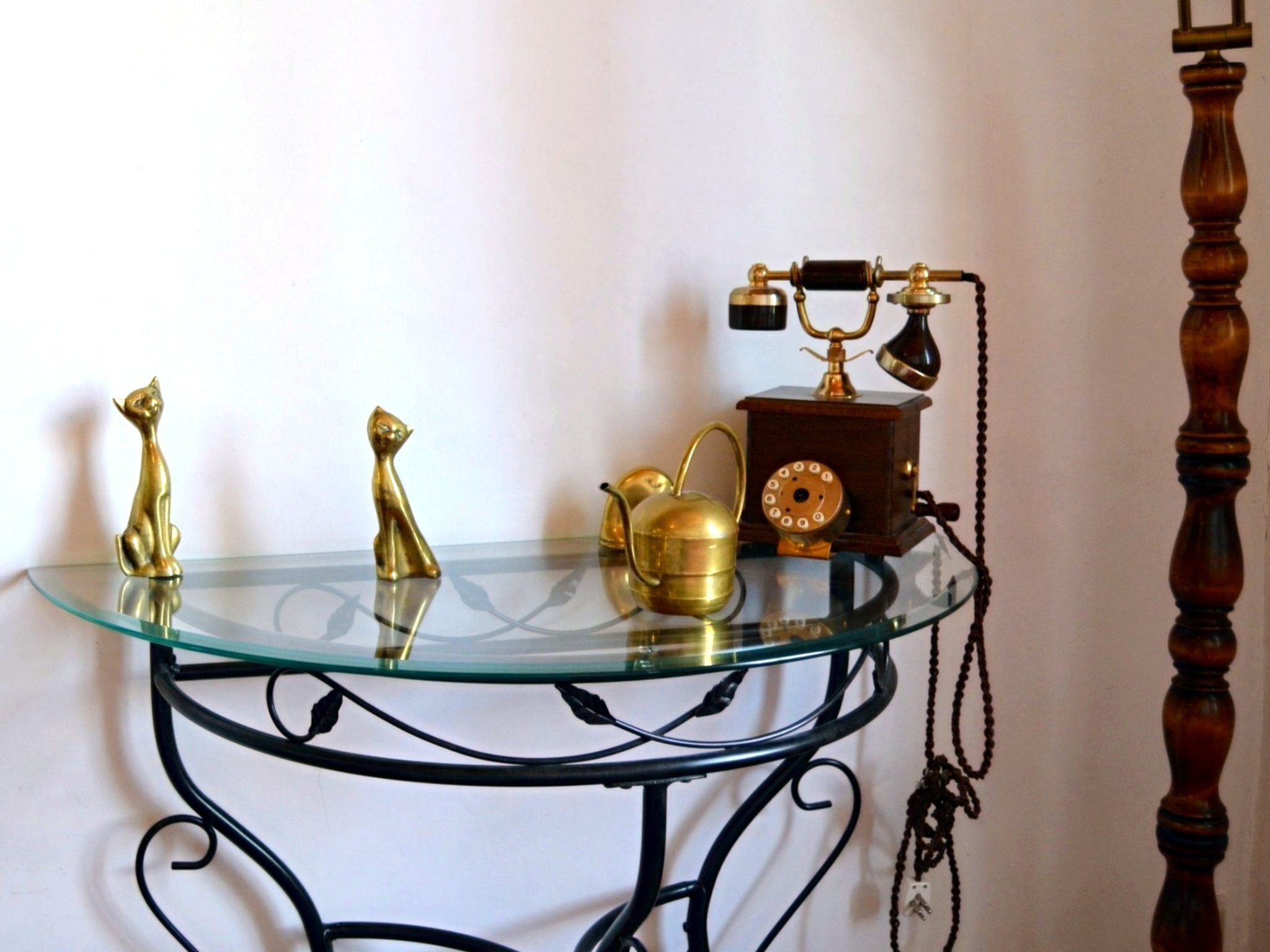 A glass-top table with a metal frame, a brass telephone, a brass teapot, and two brass cat figurines.