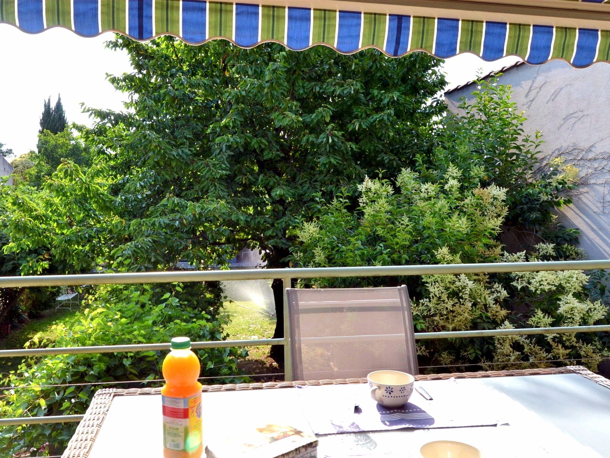 Ein Balkon mit Tisch, Stuhl und einer Flasche Orangensaft.