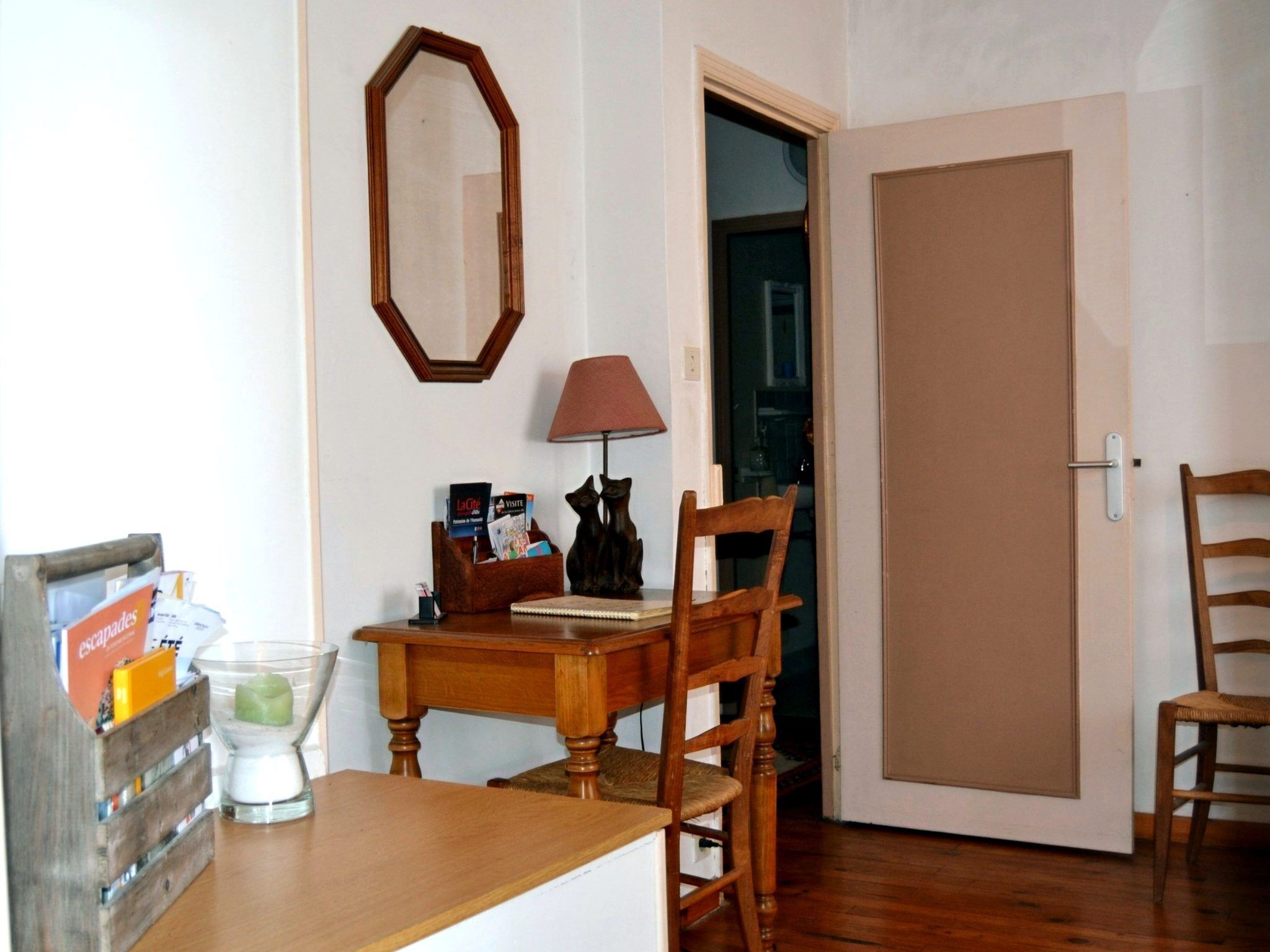 Una habitación con una mesa de madera, una silla, una lámpara, un espejo y una puerta.