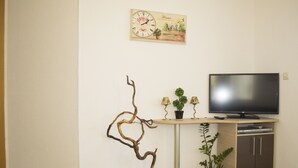 A living room with a television, a small table with lamps, a potted plant, and a wall clock. - Exclusive Apartment Tiffany Ohrid (Ohrid)