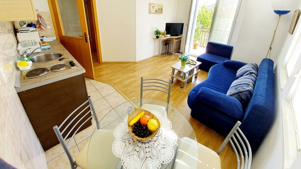 A compact living space with a kitchenette, a dining area with a table and chairs, a blue sofa, and a TV. - Exclusive Apartment Tiffany Ohrid (Ohrid)