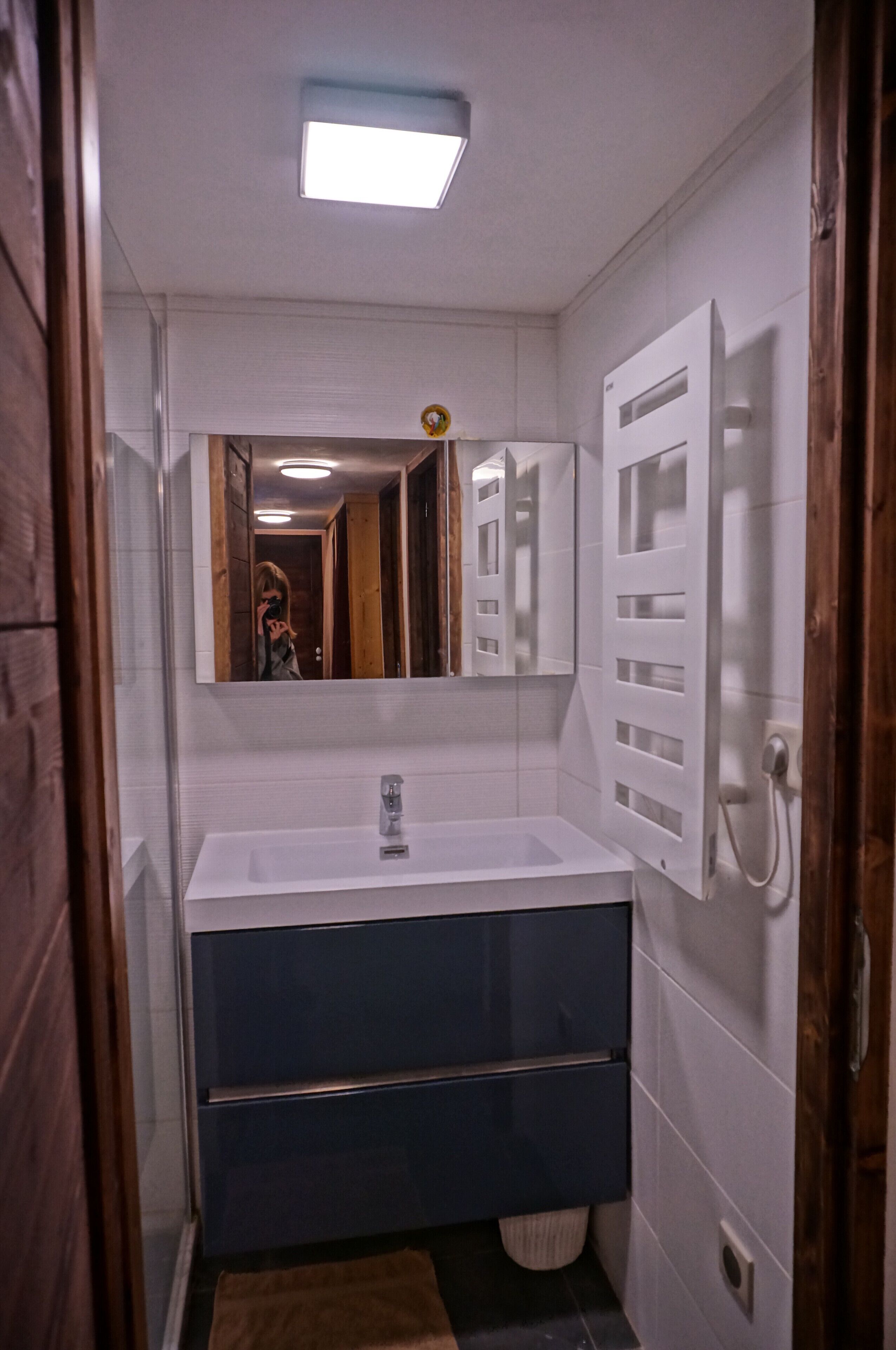 Ein Badezimmer mit einem weißen Waschbecken, einem dunkelblauen Schrank und einem Spiegel darüber.